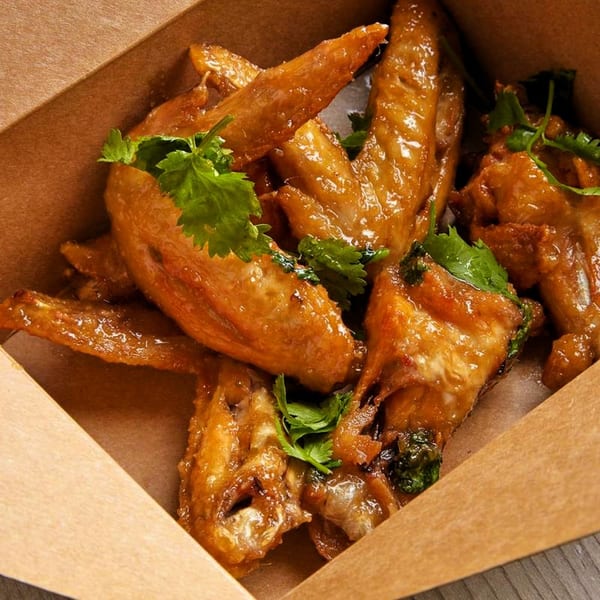 Burd Chicken Rice's glazed chicken wings with cilantro in a brown takeout box.