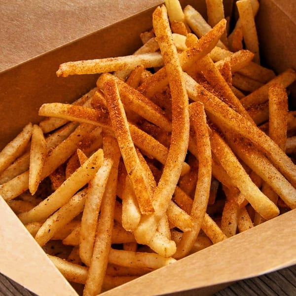 Close-up of golden french fries seasoned with spices, served in a brown paper container.